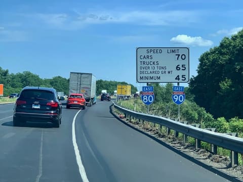 A white speed limit sign beside I-80 and I-90 East: cars 70, trucks over 13 tons declared gross weight 65, minimum 45.