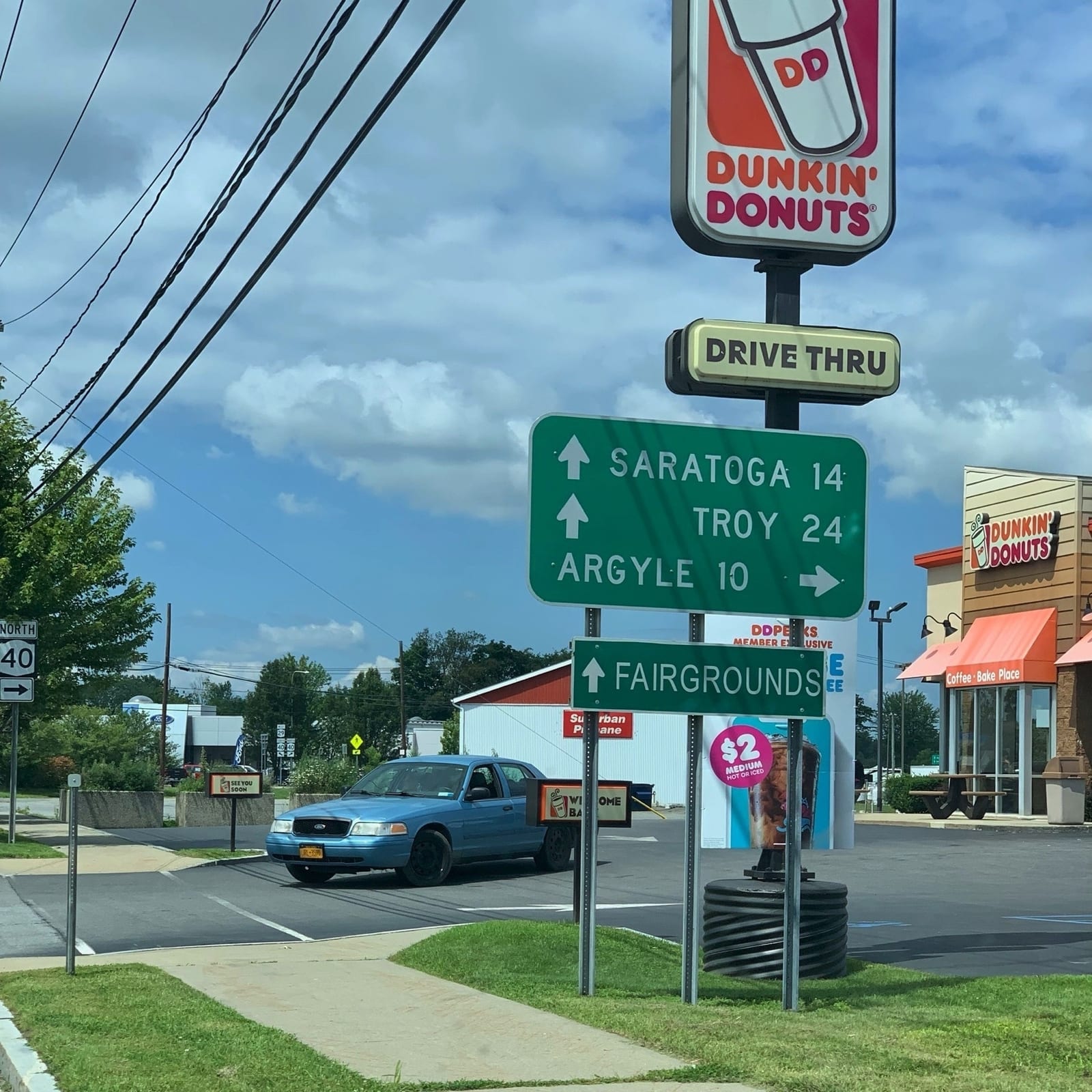 A green sign at a corner by a Dunkin' Donuts: Saratoga 14 and Troy 24 ahead, Argyle 10 to the right.