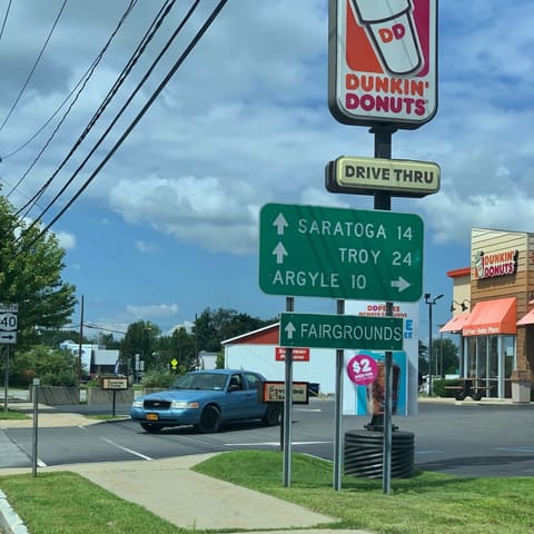 A green sign at a corner by a Dunkin' Donuts: Saratoga 14 and Troy 24 ahead, Argyle 10 to the right.