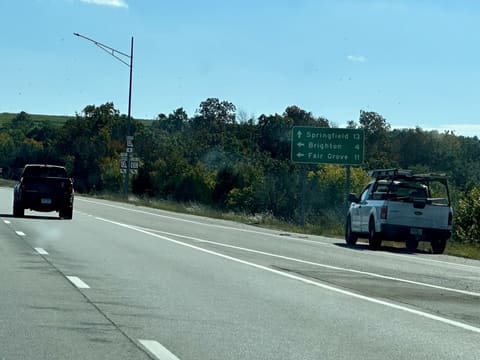 A green sign beside the highway: Springfield 13 ahead, Brighton 4 and Fair Grove 11 to the left.