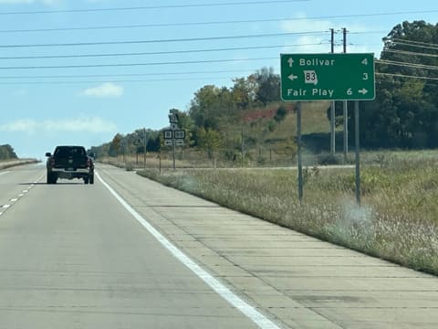 A green sign beside the highway: Bolivar 4 ahead, Missouri 83 3 to the left, Fair Play 6 to the right.