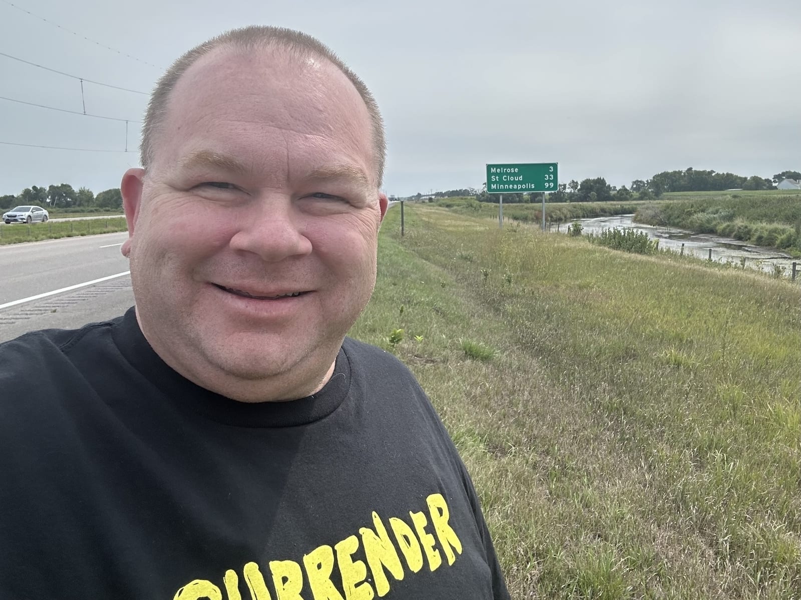 A selfie at the roadside with the Melrose, St Cloud and Minneapolis sign behind.