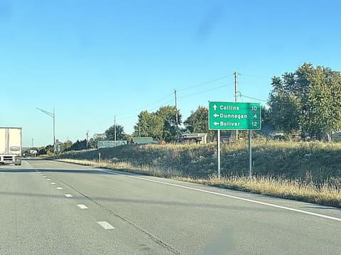 A green sign beside the highway: Collins 10 ahead, Dunnegan 4 and Bolivar 12 to the left.