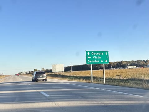 A green sign beside the highway: Osceola 5 ahead, Vista 1 to the left, Gerster 6 to the right.
