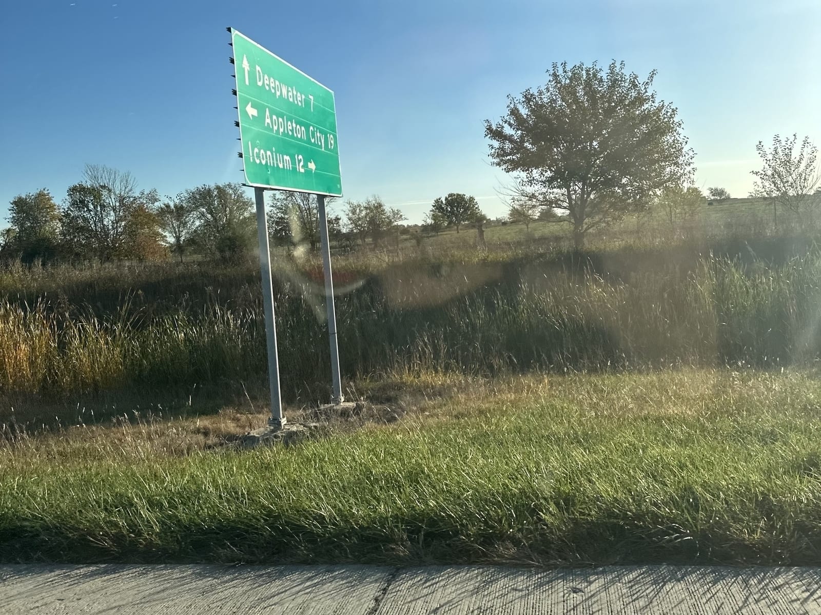 A green sign in a field: Deepwater 7 ahead, Appleton City 19 to the left, Iconium 12 to the right.